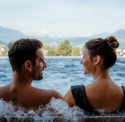 Paar im Wasserbecken mit Massagedüsen des Wellnesshotels in Oberösterreich mit Blick auf die Berge