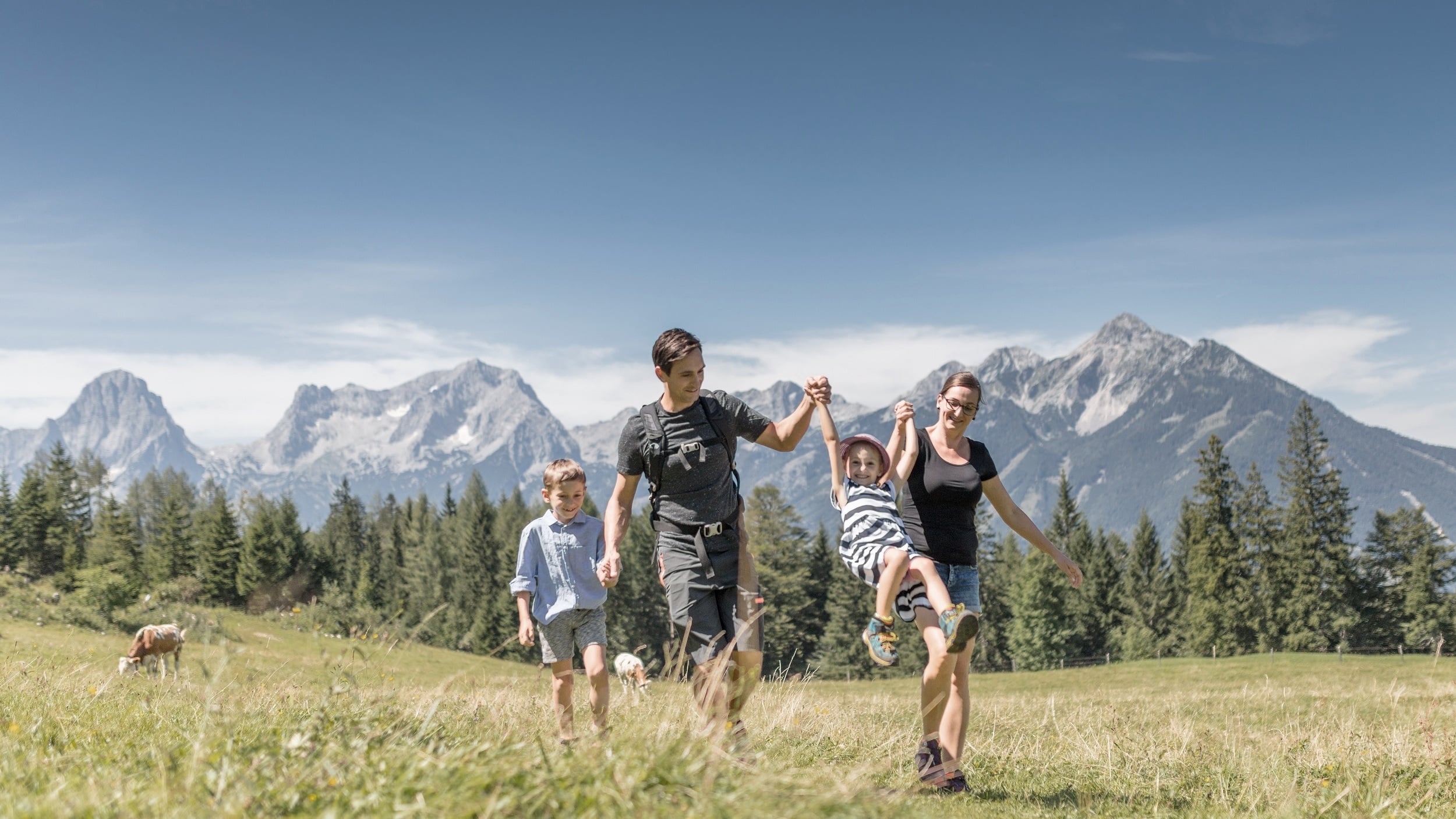 Family with children hiking in a meadow in front of the mountains in summer