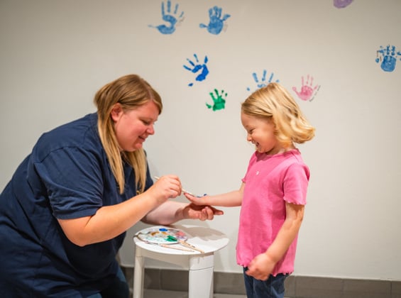 Frau bemalt die Hand eines kleinen Mädchens mit Farbe