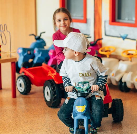 Two small children on tricycles in the indoor playground at the family hotel in Upper Austria