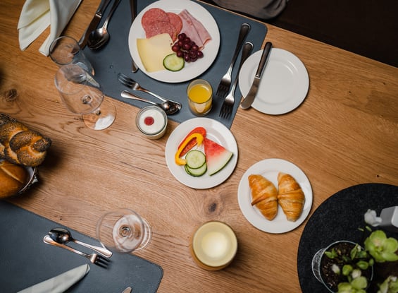 Gedeckter Frühstückstisch mit Wurst, Käse, Gemüse und Croissants