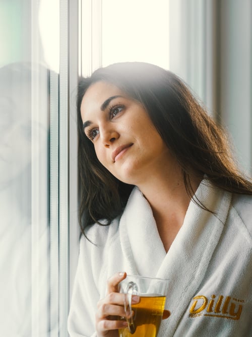 Woman with tea in a bathrobe looks dreamily out of the window