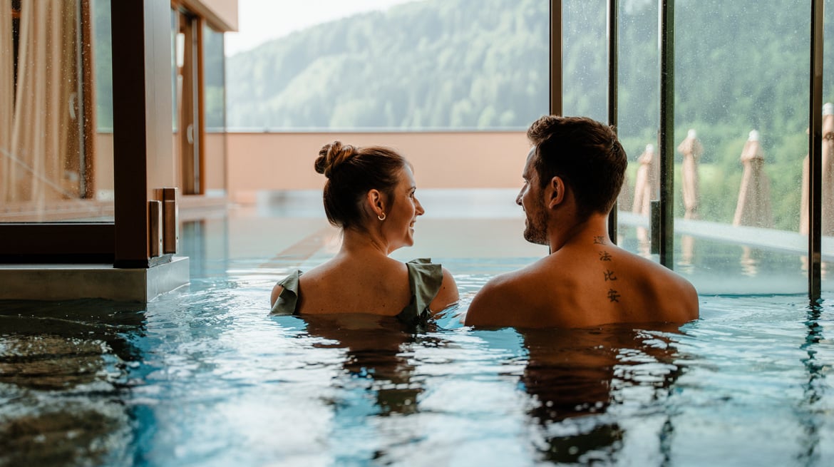 Couple from behind in the indoor pool in front of panoramic window