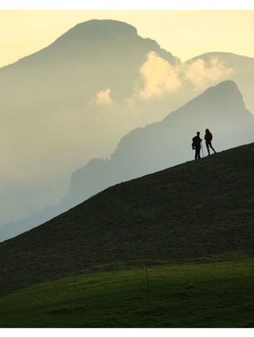 Zwei Personen stehen auf einem Hügel vor den Bergen