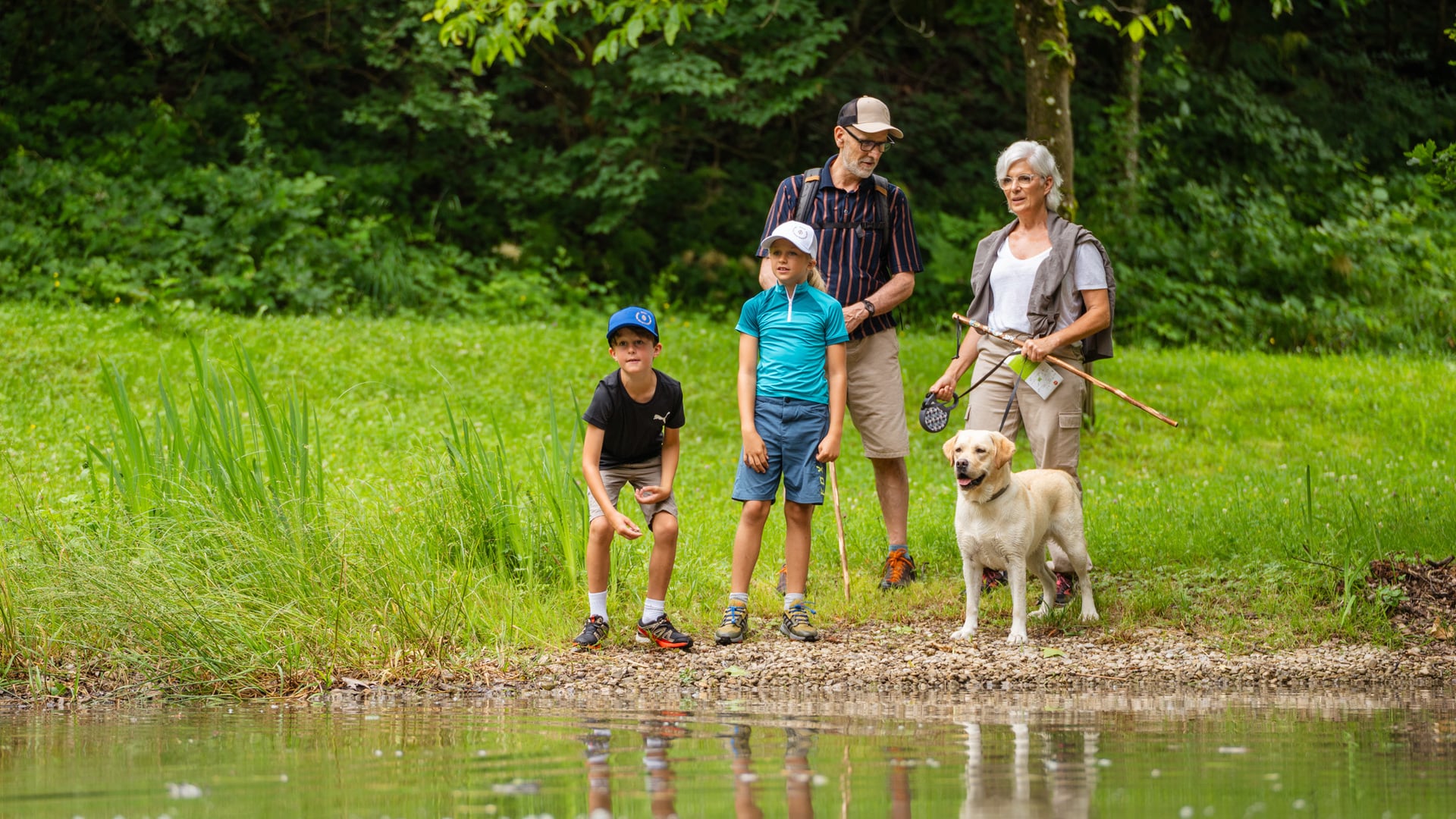 Familie steht mit Labrador vor Teich im Wald