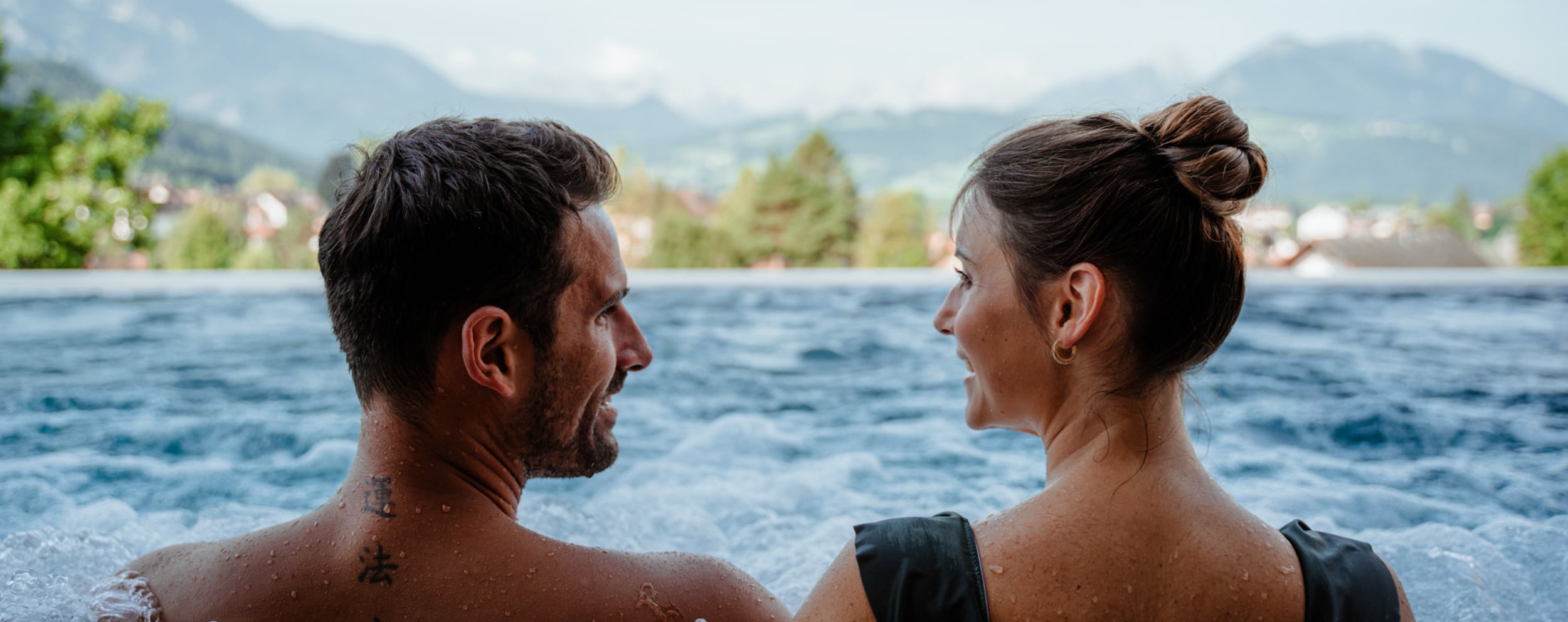 Paar sitzt bei Massagedüsen im Außenpool mit Blick auf die Berge