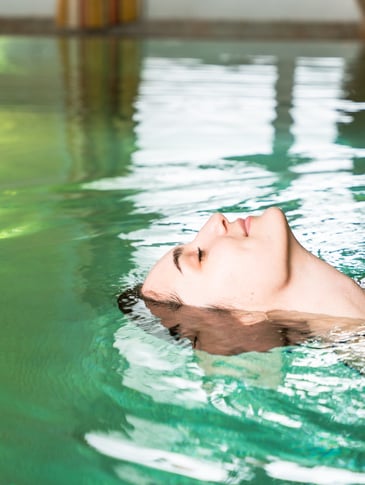 Frau liegt entspannt im Wasser im Innenpool